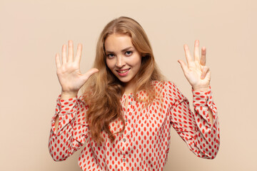 blonde woman smiling and looking friendly, showing number nine or ninth with hand forward, counting...