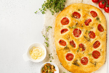 Homemade traditional Italian bread baking with cherry tomatoes, parmesan and rosemary on rustic light table background. Top view.