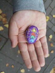 Kinderhand mit bunt bemaltem Stein im Herbst auf grauem Straßenpflaster in Oerlinghausen bei...
