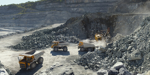 Excavator and heavy mining dump trucks in a limestone quarry, loading of stone ore, industrial...