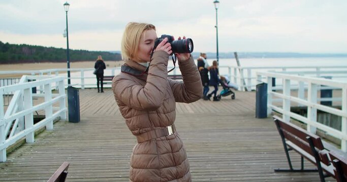 Pretty woman photographer stands in front of a beautiful seascape background with professional photo equipment. Woman with short hair and white hair is taking pictures of the landscape. Slow motion