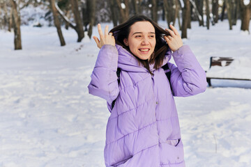 A female in a purple down jacket walks in the park in winter and enjoys the snow