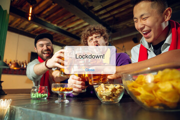 Cancellation. Soccer, football fans with snacks cheering for favourite sport team in bar, behind the message with word Lockdown. Look excited, shocked, highly tensioned. Blocked social life.