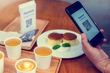 Hand using smart phone to scan QR code on tag with blurry dessert and tea in coffee shop to accepted generate digital pay without money. Qr code payment concept.