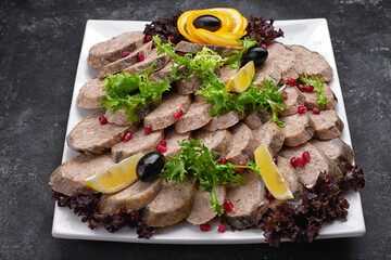 Banquet serving menu stuffed fish cut into slices with lemon and olives on a dark background on a white plate