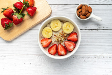 Oatmeal Porridge with Strawberries, Almonds and Banana in white bowl. Healthy Breakfast with Oatmeal and Fresh Organic Strawberry. vegan food. healthy food concept