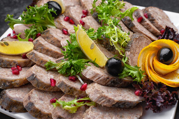 Banquet serving menu stuffed fish cut into slices with lemon and olives on a dark background on a white plate