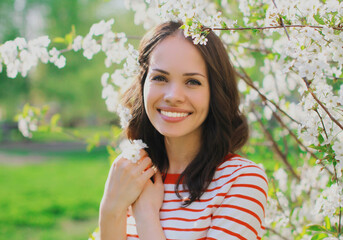 Portrait close up of lovely young woman in a spring blooming garden on a white flowers background