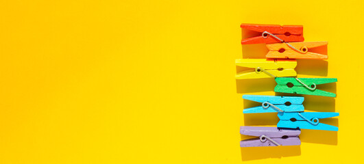 Banner concept of mood-boosting color, multi-colored wooden multi-colored clothespins on a yellow...