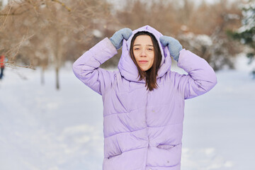 an emotional female in a purple down jacket enjoys the snow in the park