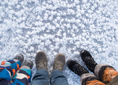 Love Winter . 3 pairs of feet, mom, dad and little son in winter shoes stand in snow near beautiful ice flowers created by nature. Rest in the winter season, active lifestyle. Empty space for text