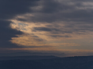 Silhouette of popular historic Hohenzollern Castle on the foothills of low mountain range Swabian Alb below dramatic brightening sky of orange colored clouds viewed from Wurmlingen, Germany in winter.