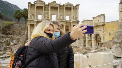 Traveling during the Covid-19 pandemic. A woman in a mask takes a selfie photo against the backdrop of attractions. Ruins of the ancient Greek city of Ephesus in Turkey. Taking pictures of himself.