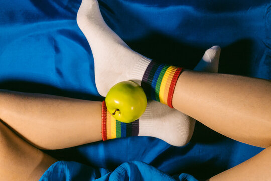 Human legs with rainbow socks and a green apple