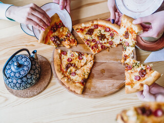People hands taking slices of pizza. Pizza and hands close up on the table. view from above