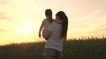 A farmer mom carries a child in her arms through wheat field. Mom plays with her little daughter at sunset. Mom walks with the baby in the fresh air. Happy family lit by the sun