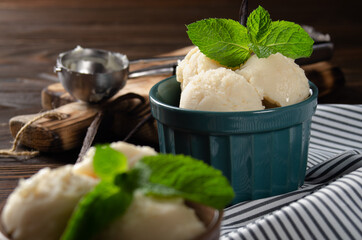 Vanilla icecream balls in clay bowls on wooden kitchen table with ice cream scoop aside
