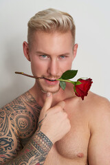 Closeup of a male lover with a flower in the mouth / Face of a handsome young man holding a red...