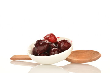 Several sweet organic pitted frozen red cherries in a white saucer with a wooden spoon, close-up, isolated on white.