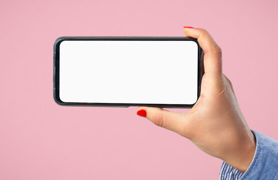 A woman's hand holds a smartphone with a blank white screen horizontally. On a pink background.