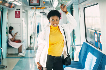 A smiling young African woman holds on to a handrail while standing on a subway train during her daily commute to work