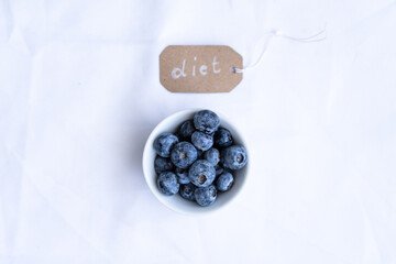 Blaubeeren in einer Schüssel und ein Etikett mit dem Text in englisch diet auf einem weißen Tischtuch. Draufsicht, gesunde Ernährung.
