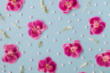 Creative and colorful floral pattern made of pink orchids and leaves on pastel blue background. Trendy flat lay.