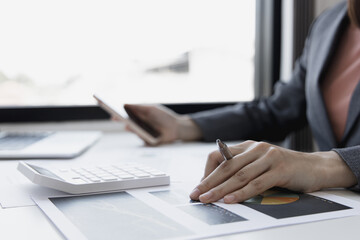 Asian female employees are analyzing market data via smartphones and have laptops to calculate the company's finances In a private office at home, Working at home and new normal concept.