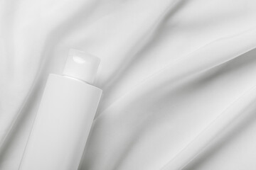 Cosmetic bottle tube packaging on white silk fabric background. Beauty and skincare concept, mockup for design. Minimal monochrome color composition. Top view, flat lay, copy space