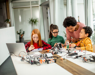 Happy kids with their African American female science teacher with laptop programming electric toys and robots at robotics classroom
