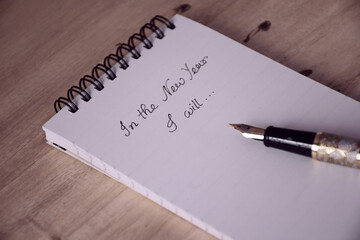 Close-up of notepad with handwritten message and fountain pen on wooden desk. Selective focus on the text. New Year plans, goals and actions, conceptual image with faded tone.