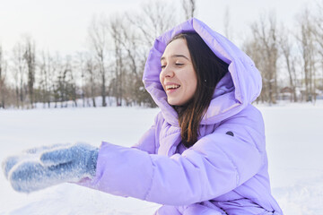 an emotional female in a purple down jacket enjoys the snow in the park