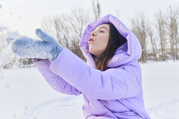 Fototapeta na wymiar an emotional female in a purple down jacket enjoys the snow in the park