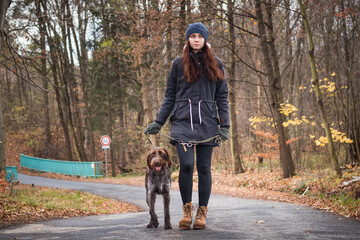 smiling authentic girl with her dog Bohemian Wire-haired Pointing Griffon breed is walking through nature. Candid portrait of young woman with man's best friend. Binary portrait in nature
