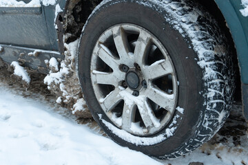 Parts of the car are covered with snow and ice after a snowfall. Wheel close-up in dirt and anti-icing reagents. Big frosts and a lot of snow in the city. Problems on winter slippery roads.