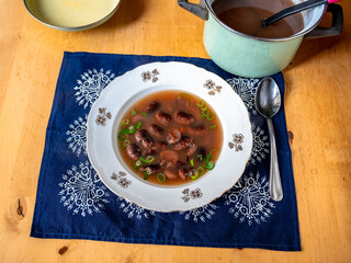 Plate with big bean soup, pot, ladle and spoon on wooden table.