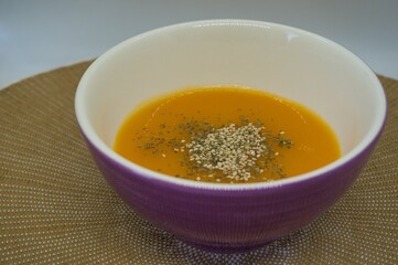 pumpkin cream with sesame and spices into a violet bowl in natural fiber background. Healthy food concept