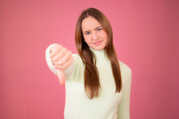 Beautiful girl with long hair with thumb down gesture over pink background