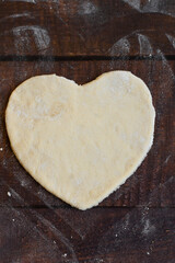 Bakery items - uncooked yeast dough in heart shape on wooden flour background