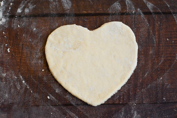 Bakery items - uncooked yeast dough in heart shape on wooden flour background