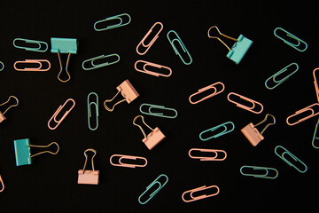 Paper clips and clips in blue and pink are scattered on a black background. Office supplies. Background and texture.