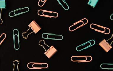 Paper clips and clips in blue and pink are scattered on a black background. Office supplies. Background and texture.