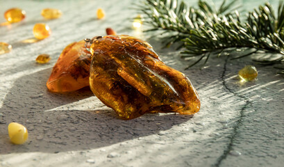 Baltic amber pendant lying on an amber stone on a gray plastered surface with water drops close up.
