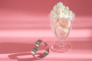 Sweet marshmallows in the glass with a heart and pink background. Holiday food concept.