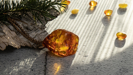 Sparkling yellow orange Baltic amber pendant with water drops on a birch bark. Amber jewelry is in the sunlight.  