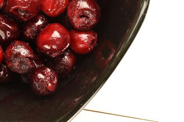 Several organic frozen pitted red cherries in a black dish on a white table, close-up, top view.