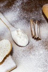 Flour in a wooden spoon, sliced French baguette on a wooden board and cinnamon sticks heavily floured on a wooden table. Side view with place for text or logo.
