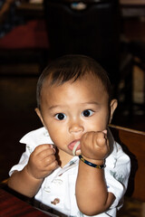 Adorable Filipino American baby eating noodles by hand.