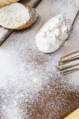 Sliced French baguette on a wooden board, cinnamon sticks and a trail of a large spoon, heavily floured on a wooden table. Top view with place for text or logo.