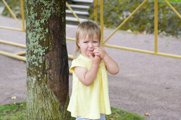 Little blonde baby girl in a yellow dress crying in the park.  Sad, depressed and upset girl cries outdoor. Tantrums and whims of children. Child emotions and capricious. Emotional Disorders